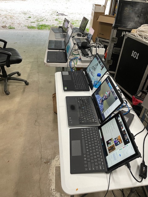 7 laptops lined up on 2 tables playing different videos