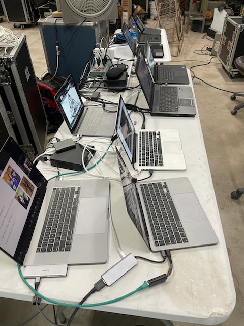 sideshot of 6 laptops oprn on a table, playing different videos